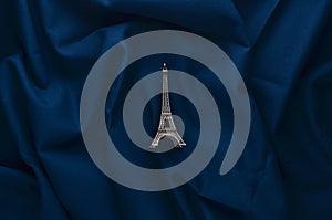 A miniature statuette of the Eiffel Tower on a dark blue cloth background. Souvenir from Paris. Trend minimalism.