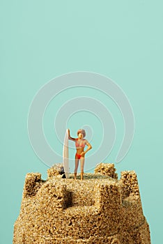 Miniature surfer woman on a sandcastle