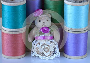 Miniature teddybear dressed in lace and roses with spools of thread as background. photo