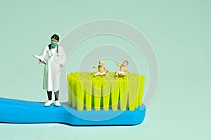 Miniature tiny people toy figure photography. Two boy infant toddler whimpering, seat above toothbrush beside women doctor.