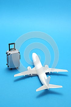 Miniature toy airplane and suitcase on blue background.