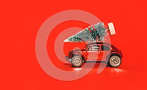 Miniature toy artificial Pine tree on wooden base and red car, bright red Christmas background with long shadow overlay