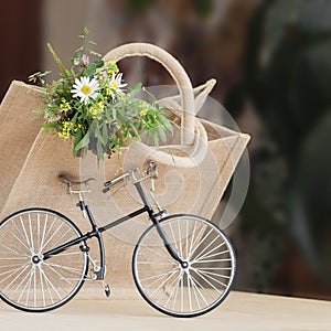 Miniature toy bike and flowers bouquet in canvas bag, closeup concept of country summer and leisure