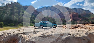 Miniature toy car perched atop a large rock, with majestic mountain peaks in the distant background