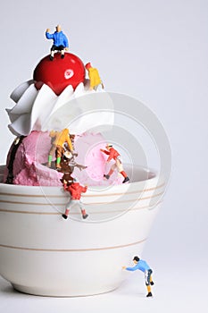 Miniature, toy climbers ascend a small bowl of ice cream.