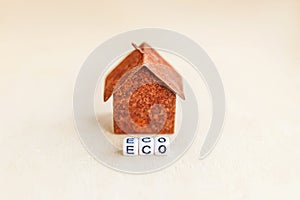 Miniature toy model house with inscription ECO letters word on wooden backdrop. Eco Village, abstract environmental background.