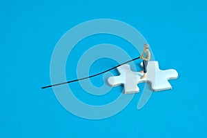 Miniature toy photography people. Fisher standing above white puzzle jigsaw piece. Isolated on blue background