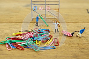 Miniature toy workers carry a paper clip