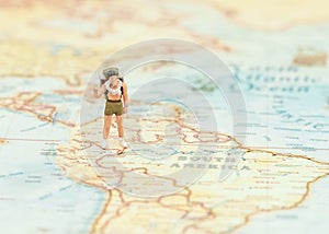 Miniature traveler man with backpack standing on wold map for travel around the world.