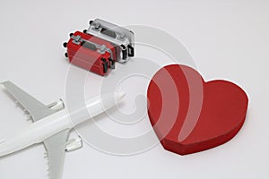 Miniature two suitcases, toy airplane, and a red heart on white background.