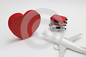Miniature two suitcases, toy airplane, and a red heart on white background.