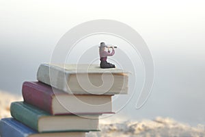 Miniature woman looks at the infinity with the spyglass on a scale of books photo