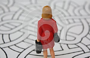 Miniature woman in red coat from behind in the maze. Lost or confused lady decides, which way to go