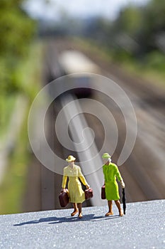 Miniature women with luggage standing on a platform ready to travel