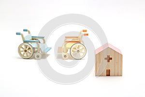 Miniature wooden hospital and wheelchairs on white background.