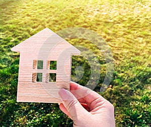 Miniature wooden house on green grass in female hands. Real estate concept. Modern housing. Eco-friendly and energy efficient