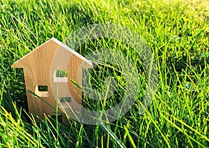 Miniature wooden house on green grass. Real estate concept. Modern housing. Eco-friendly and energy efficient house. Buying a home