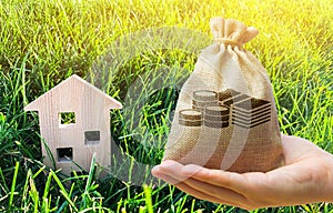 Miniature wooden house and money bag on grass. Real estate concept. Eco-friendly and energy efficient house. Buying a home outside