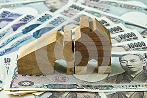 miniature wooden house on pile of japanese yen banknotes as financial or real estate mortgage concept