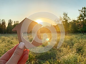 Miniature wooden house in the shape of a heart in the hands of a girl outdoors. Real estate concept. Eco-friendly home. Buying a