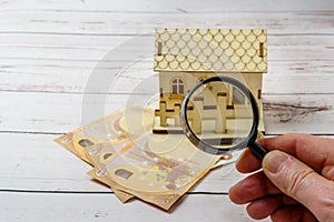 Miniature wooden house surrounded by euro banknotes. Savings concept for house purchase. Rise in mortgage interest rates