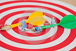 Miniature worker toy on red dart board with green dart