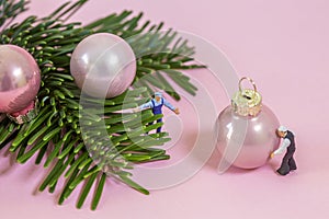 Miniature workers decorating a branch of pines with christmas balls