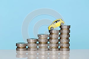 Miniature yellow car model on growing stack of coins money on blue background, Saving money for car, Finance and car loan,
