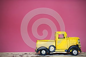 Miniature yellow toy car on wood table pink wall background.