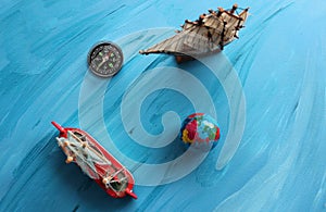 Miniatures on the theme of sea travel. Compass And Small Globe Near Sailing Ships Model On Blue Painted Surface