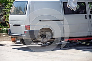 Minibus with rear wheel removed, lifted by hydraulic jack, car repair next to service garage. Rear back view