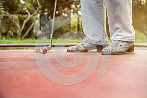 Minigolf player starts to hit a billard looking cue ball at the