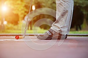 Minigolf player tries to put a ball into the hole at a sunny day