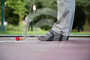 Minigolf player tries to put a red ball into the hole at a sunny