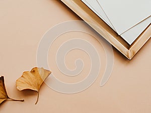 Minimal aesthetic composition with golden tray and whitre cards and two yellow leaves on beige background