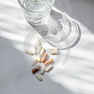 Minimal beauty, wellness, pharmaceutical industry concept. Different pills, capsules, glass with pure water on neutral white