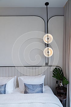 Minimal bedroom corner with circular wall lamp installed on the wall with beige wallcovering in natural light setting scene /