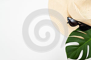 Minimal composition with beach straw hat, sunglasses and tropical Monstera palm leaf on white background. Flat lay, top view,
