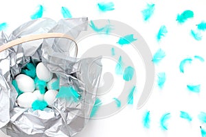 Minimal composition for Easter. basket decorated with silver paper, white eggs and turquoise feathers. flat lay, top view