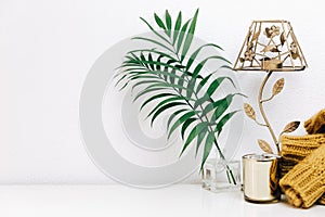 Minimal composition with green tropical leaves, candle and trendy warm sweater