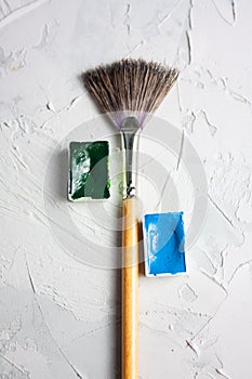 Minimal composition with paint brush and watercolor blue and green cuvettes on a white on concrete, plastered background