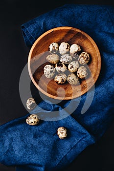 Minimal concept of fresh quail eggs in the wooden bowl on the dark background with blue saten or silk around