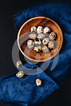 Minimal concept of fresh quail eggs in the wooden bowl on the dark background with blue saten or silk around photo