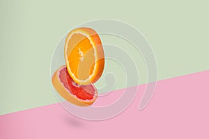 Minimal creative  idea with fresh flying orange and grapefruit piece on a light green and pink background