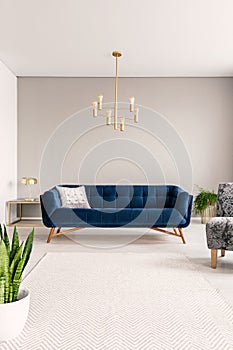 Minimal living room interior with a blue sofa and lots of empty space on the floor and on the background wall. Real photo.