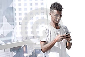 Minimal looking portrait of young African Black man, he is texting a message with a mobile phone in a modern office, elegant image