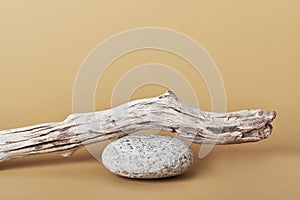 Minimal natural product display on beige background. Stone pebble podium and weathered driftwood. Showcase concept