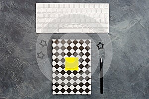 Minimal office concept. Keyboard, lack paper clips, bright yellow sticky note and pen and closed black-white colored