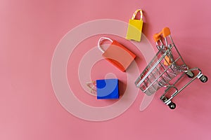 Minimal shoping online concept, Colorful paper shopping bag and trolley go down from floating pink background for copy space