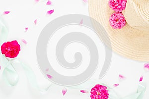 Minimal style composition with beach straw hat, pink rose flowers bud and petal and blue mint ribbon on white background. Flat lay